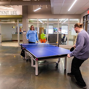 Two students playing ping pong in commons area