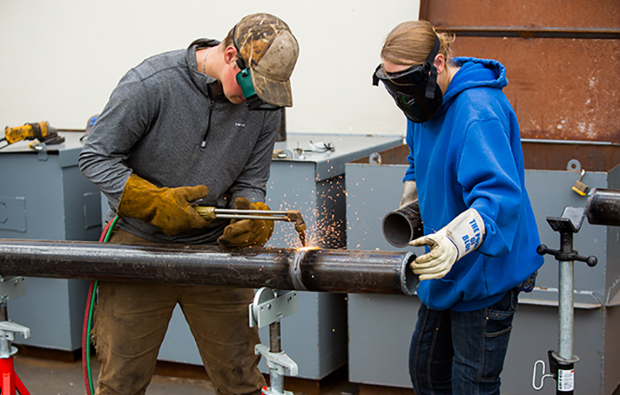 Two students welding a pipe