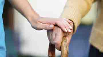 Close up of a hand on a cane and a caregiver's hand gently on top of the other hand