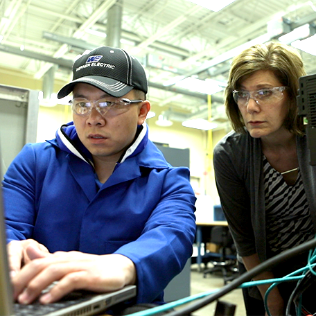 A student working on a computer with the instructor watching
