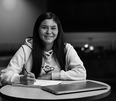 Student looking at the camera smiling with paper and laptop on table