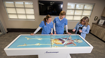 Students view a body on the anatomage table