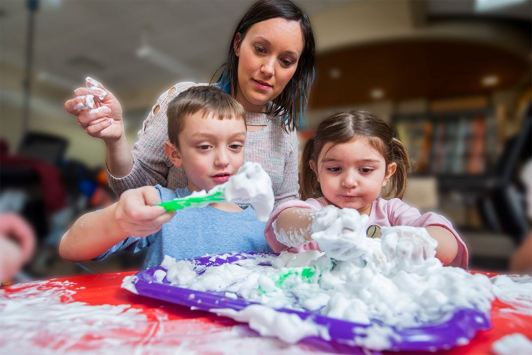 Childcare provider working on a shaving cream craft with two elementary aged children