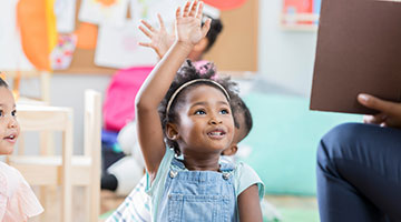 Preschool-aged kid raising their hands in a classroom