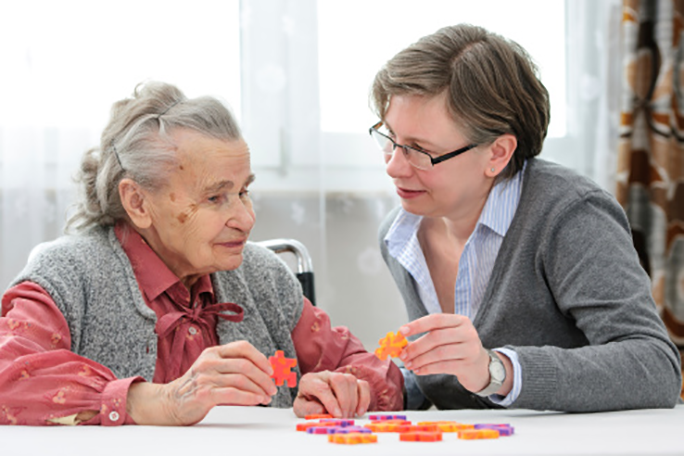 A personal care worker assisting an aging adult with a puzzle