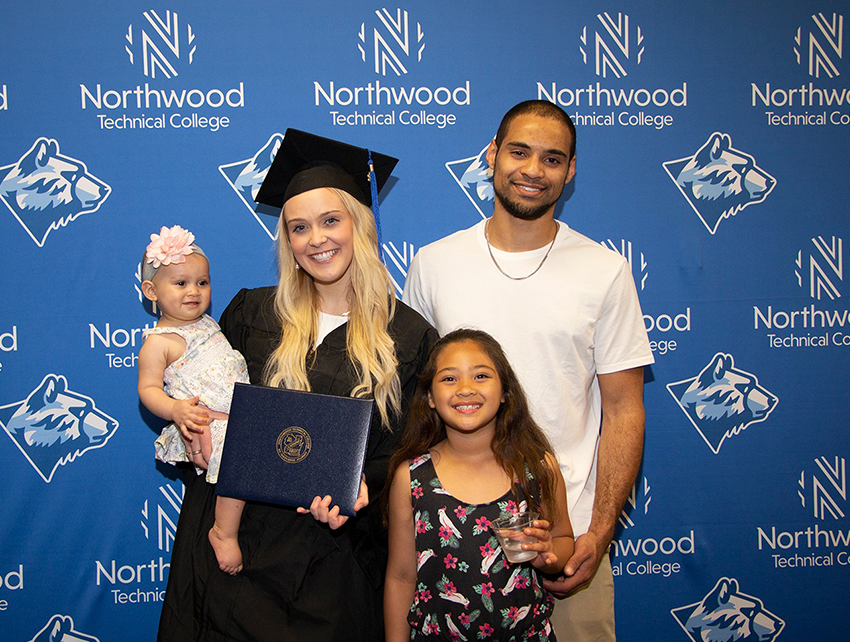 Scholarship recipient standing in front of Northwood Tech backdrop with family