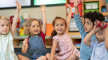 Preschool-aged kids raising their hands in a classroom