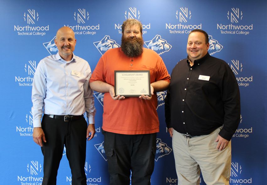 Student standing in between two Northwood Tech associates and holding a scholarship plaque.