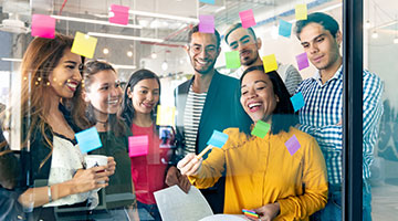 Young professionals planning tasks on glass wall with adhesive notes