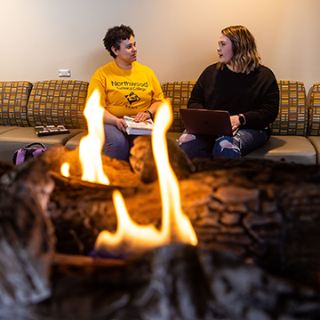 Two students sitting by a fireplace in a common area on campus
