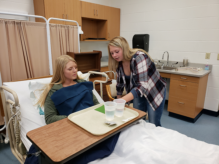 Nursing assistant students practicing helping a patient in hospital bed
