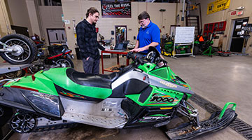 A student and instructor looking over a snowmobile in the lab