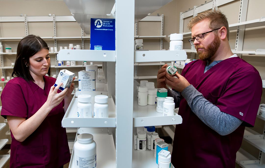 2 pharmacy technicians looking at shelves of medications