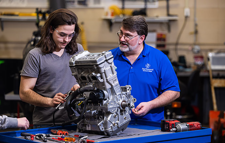 A student working on a small engine with instructor supervision in the power sports lab on campus