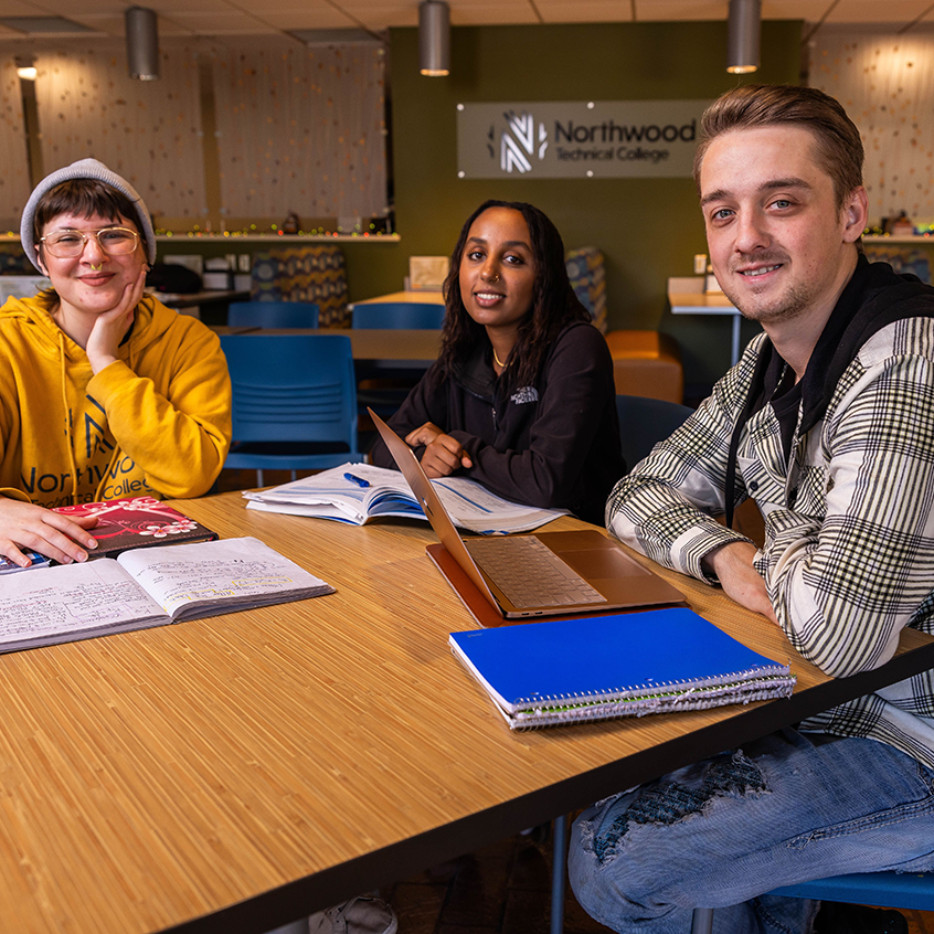 Three students studying in the commons area smiling at the camera