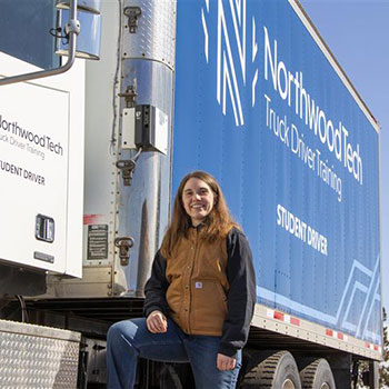 A female truck driving student standing outside of the cab of a semi truck