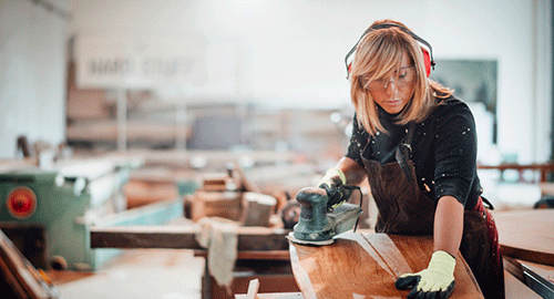 Female carpenter using an orbit sander to sand down a wooden panel