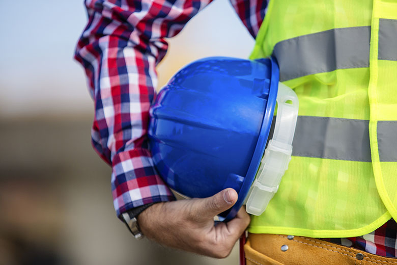 Worker in yellow safety vest holding blue hardhat