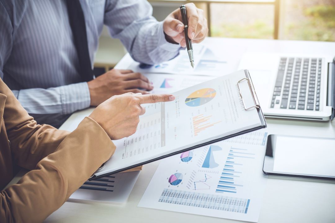 two people sitting with spreadsheets and graphs in front of them