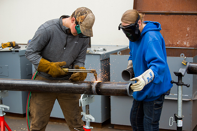 Two students welding a pipe