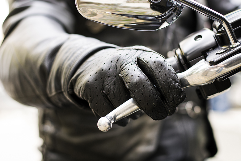 Close up of a black leather glove gripping motorcycle handlebar