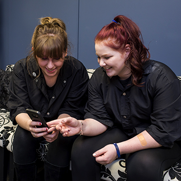 Two cosmetology students looking at a phone and laughing
