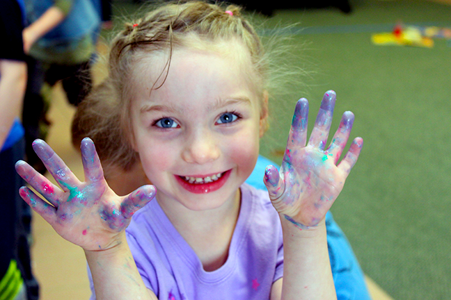 Child smiling and holding up messy and sparkly hands