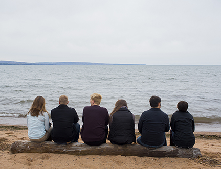 Students sitting on a log at the beach looking out toward Lake Superior