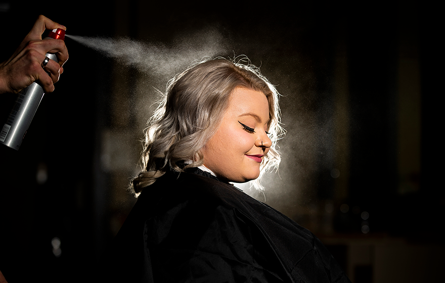 A cosmetology client having their hair sprayed